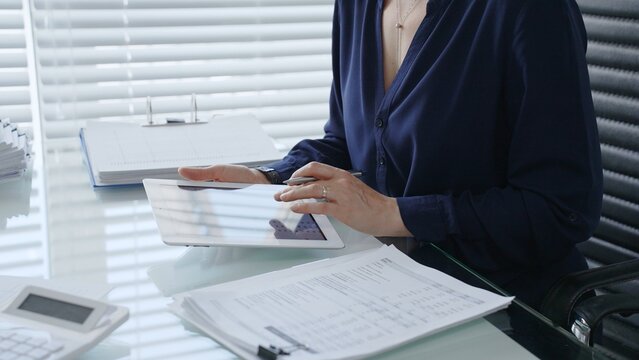 Professional woman using digital tablet for business tasks, typing data and reviewing documents at a modern office desk, symbolizing efficiency and financial management