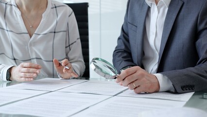 Business professionals reviewing legal contracts and important documents with a magnifying glass, performing careful examination and due diligence for risk assessment © rogerphoto