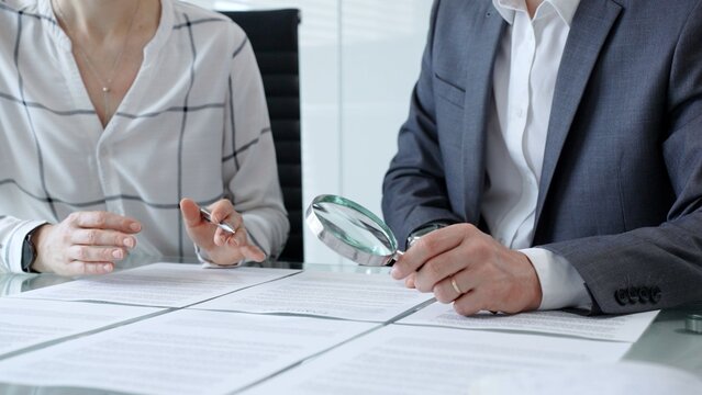Business professionals reviewing legal contracts and important documents with a magnifying glass, performing careful examination and due diligence for risk assessment