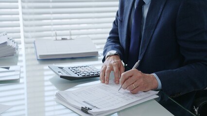 Business professional performing financial calculations and analysis using a calculator and pen,...