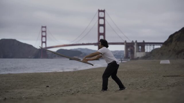 Man Tossing Large Painted Board on Beach by Golden Gate Bridge