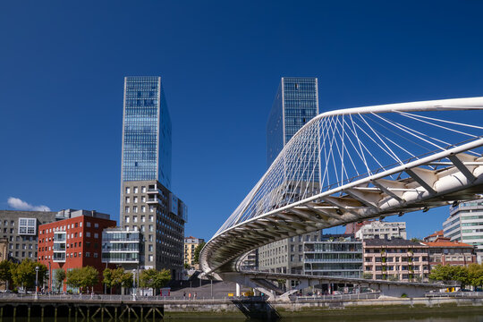 Modern architecture of zubizuri bridge over nervion river with urban buildings under blue sky