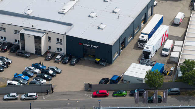 Meuspath, Germany - 23 June 2026: Aerial view of Manthey Racing GmbH headquarters featuring industrial buildings, parked cars, and transport trucks in the parking lot.