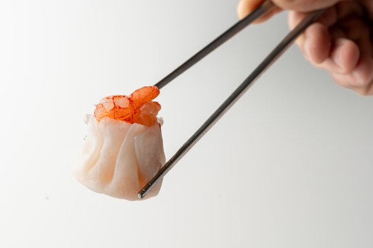 Hand holding shrimp shumai dumpling with chopsticks isolated on white background