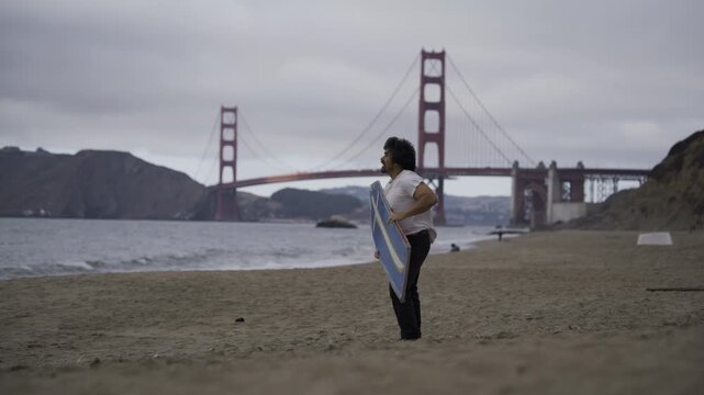 Man Spinning Large Blue Sign on Beach Against Strong Wind Near Golden Gate Bridge - Wide Shot
