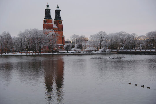 Distant view of Klosters Church with reflection in the Eskilstuna River surrounded by snow-covered trees