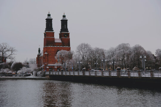Distant view of Klosters kyrka church and frosted trees across the water in winter under an overcast sky in Eskilstuna, Sweden
