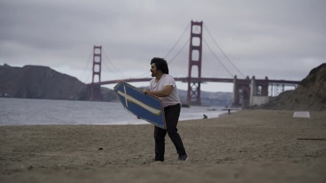 Man Releasing Painted Board into Air on Beach Golden Gate Bridge - Wide Shot