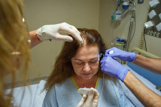 Patient undergoing sleep study, medical staff applying eeg electrodes for polysomnography in hospital