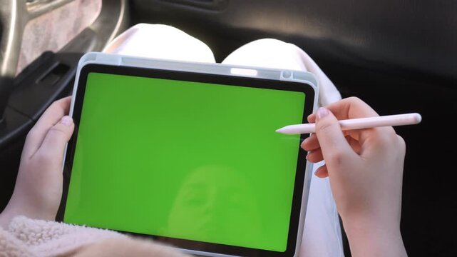 Close-up of hands holding tablet with green screen. Person draws with stylus, focused and calm. Perfect for digital art tutorials or app demonstrations. Ideal for advertising tech or creative tools