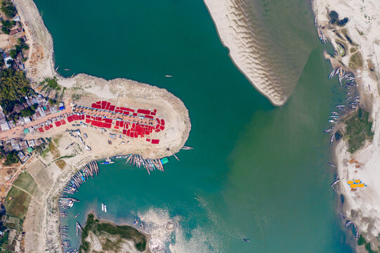 Bogura, Rajshahi Division, Bangladesh - 17 March 2024: Aerial view of Sariakandi riverbank with red fabrics drying on sand, surrounded by wooden boats moored along the river.