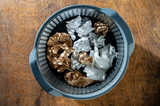 Crumpled paper balls in office trash can, top view. White and brown crumpled paper balls in grey plastic waste basket on wood desk representing brainstorm failure, waste recycling or creative crisis