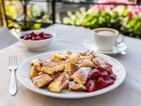 Desayuno en una terraza con panqueques y fruta en un plato junto a una taza de caf&eacute;