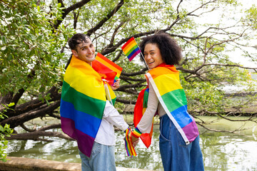 Fototapeta premium Young LGBTQ Couple Making Heart Shape with Rainbow Flags in Park