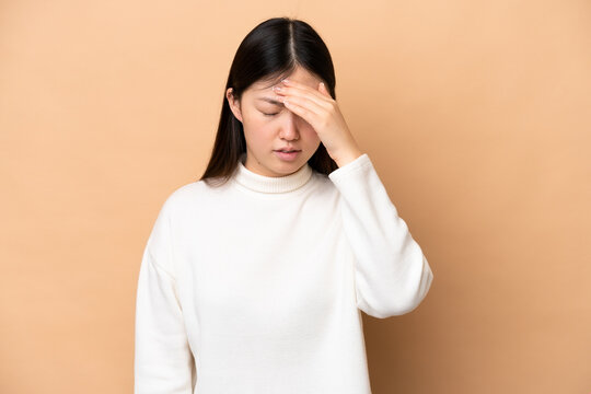 Young Chinese woman isolated on beige background with headache