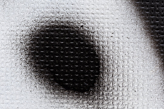 Macro close-up of a black spray painted shape on an uneven white wall. Abstract full frame textured and splattered graffiti background with copy space.