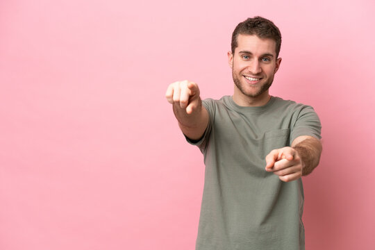 Young caucasian man isolated on pink background pointing front with happy expression