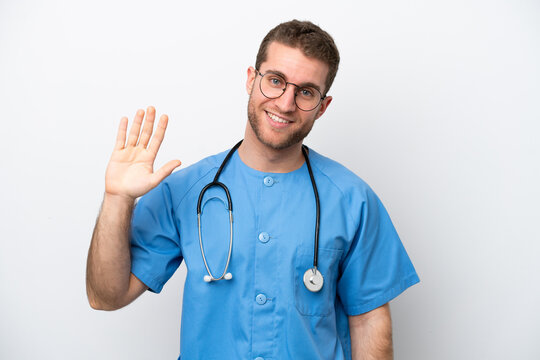 Young surgeon doctor caucasian man isolated on white background saluting with hand with happy expression