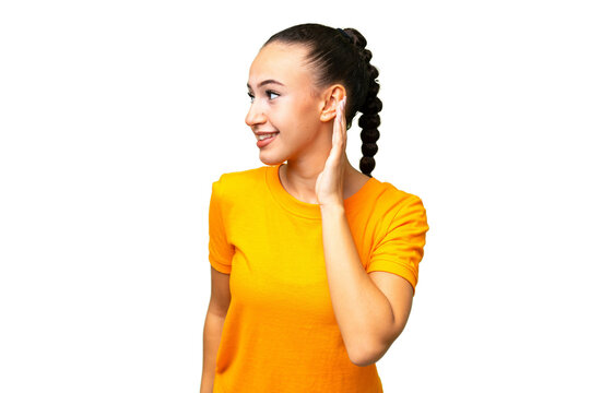 Young Arab woman over isolated background listening to something by putting hand on the ear
