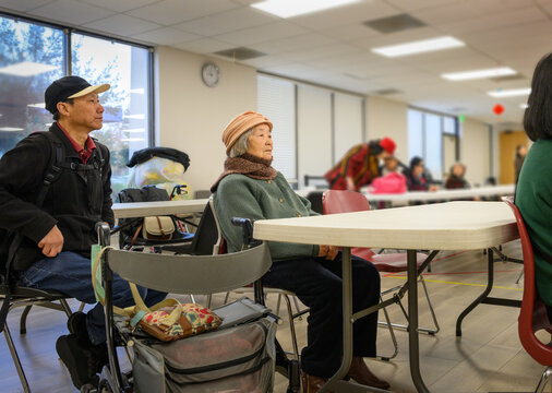 Senior woman and adult son attending a meeting in community centre. Unrecognizable senior people in the room. California. USA.