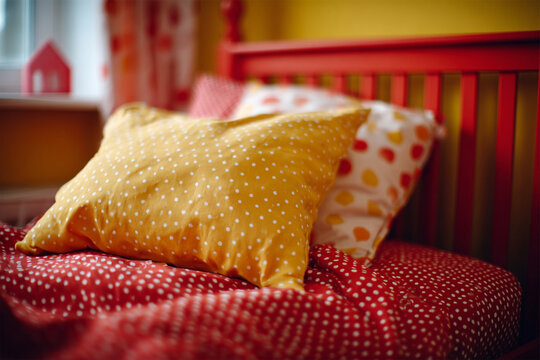 Cozy colorful bed with a red blanket and vibrant yellow pillows, close-up photo featuring modern bedroom comfort and stylish interior design