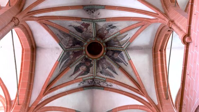 Painted angels surround a central oculus on a ribbed vaulted church ceiling in a static upward view.
