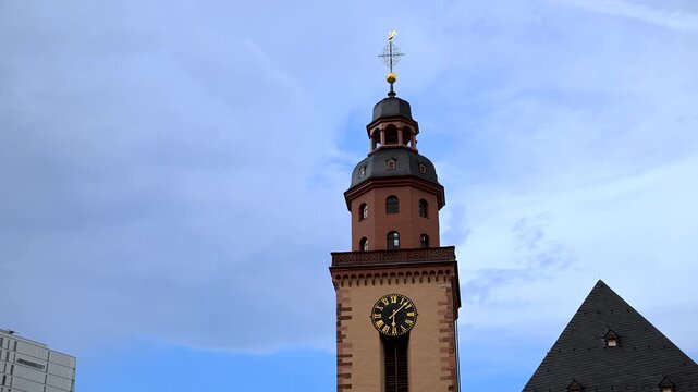 St. Catherine's Church clock tower rises beside nearby rooftops under a bright blue sky in central Frankfurt.