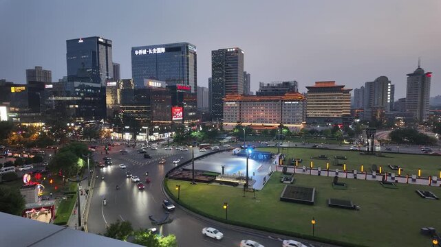 Aerial view of an urban square blending traditional and modern architecture during dusk, with roads, vehicles and green spaces.