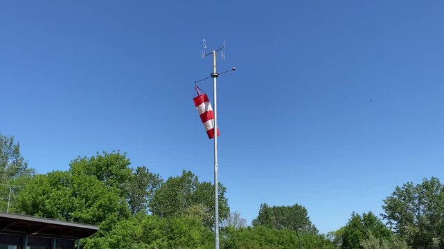 Red and white windsock blowing in the wind against blue sky background.
