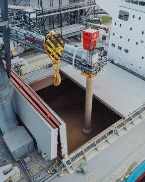 Riga, Latvia - 20 September 2021: Aerial view of a large industrial crane loading grain into the hold of a cargo ship at the port.