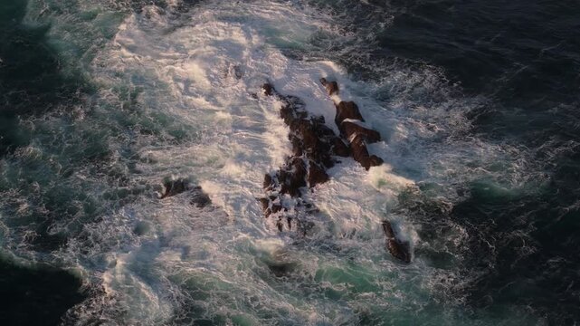 The relentless force of the waves carves patterns into the ancient rocky shore.