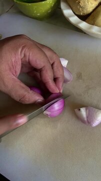 A man slicing fresh onions on a cutting board while preparing a homemade meal in a kitchen in Dhaka, Bangladesh. Everyday cooking and food preparation scene.