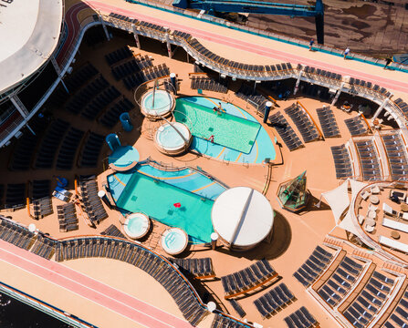 Riga, Latvia - 09 June 2022: Aerial view of the cruise ship deck featuring swimming pools, hot tubs, and rows of lounge chairs under a clear sky.