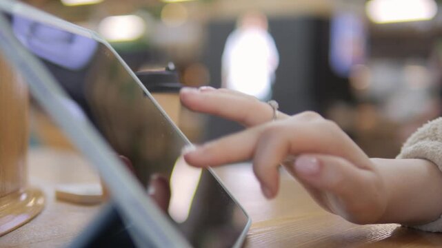 Hand taps tablet screen at cozy cafe table. Warm lighting and blurred background suggest calm focus. Ideal for digital work, coffee breaks, or tech lifestyle scenes. No identifiable expressions