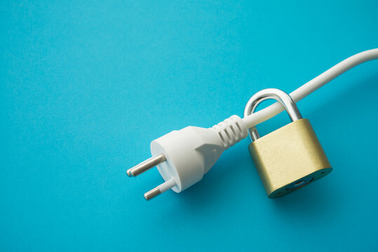 Electrical plug with padlock on blue background. Energy saving, expense control, electricity prices increase, energy crisis in war, home financial management, environmental conservation concept.