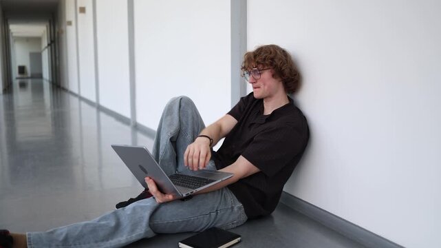 Vertical screen student sitting on corridor floor preparing for exam with laptop studying independently reviewing materials before important test