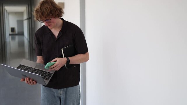 Vertical screen tired schoolboy checking laptop while holding notebook and phone overwhelmed by homework studying and endless educational tasks