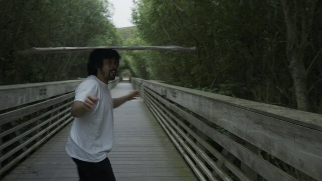 Man Throwing, Balancing and Flipping Painted Board into Air on Wooden Footbridge - Steady Cam