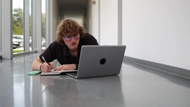 Modern student studies on the hallway floor with a laptop proving todays generation learns anywhere without worrying about what others think or where they study