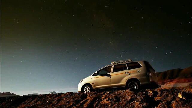A light-colored family vehicle rests beneath a vast, star-filled night sky. The scene evokes quiet adventure and peaceful contemplation under the cosmic expanse.