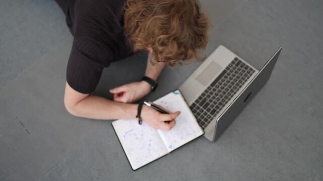 Young startup founder works from floor using laptop and notebook developing business ideas showing ambition creativity persistence and entrepreneurial mindset
