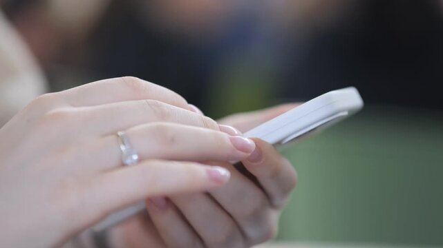 Close-up of female hands typing on smartphone. Ring visible on finger. Background softly blurred. Fingers move quickly over screen. Suitable for communication, social media, or technology themes
