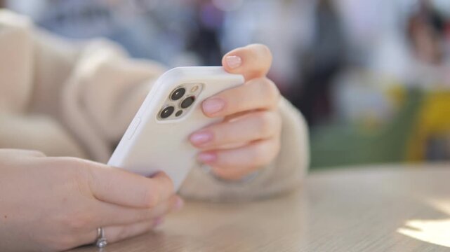 Hands holding smartphone at wooden table outdoors. Fingers tap screen, focused and calm. Perfect for social media, digital lifestyle, or communication concepts