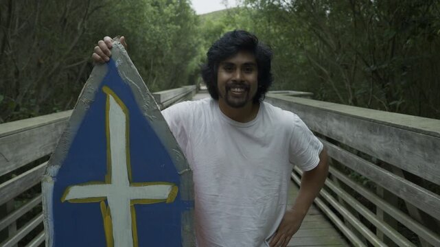 Man Holding Painted Board Upright on Wooden Footbridge - Medium, Slow Motion Shot