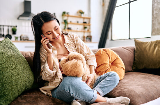 Young woman on sofa talking on phone with pet dog.