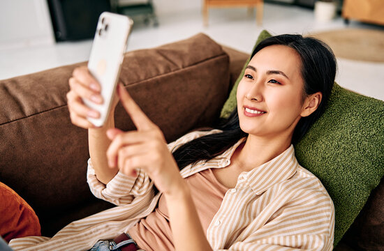 Young woman using smartphone while relaxing on sofa