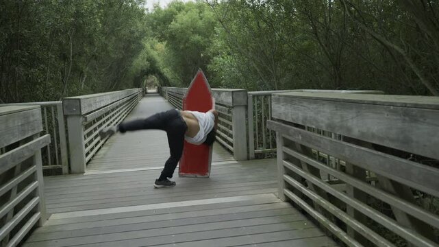 Man Swinging Large Red Arrow Sign on Wooden Footbridge And Doing flip - Wide, Slow Motion View