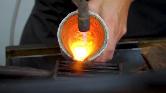 Goldsmith pouring molten metal into a graphite mold in a jewelry workshop.