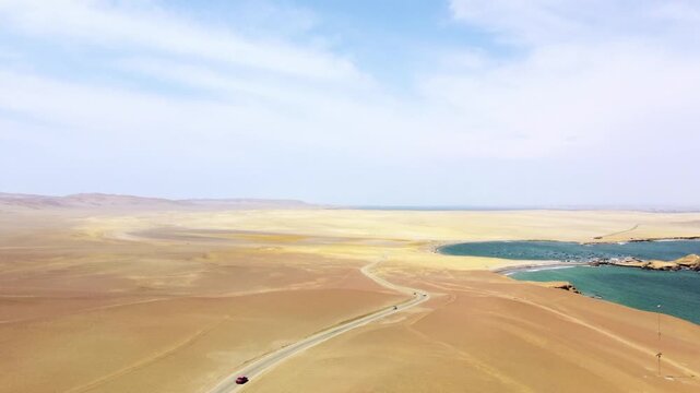 Aerial view of the arid desert landscape, winding road, and turquoise bay of the Paracas National Reserve in Paracas, Ica, Peru.