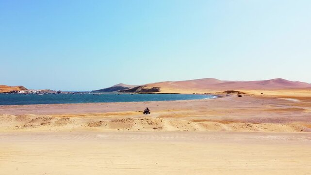 Aerial view of the arid desert landscape meeting the blue waters of the Pacific Ocean at Paracas National Reserve, with small boats anchored in the bay, Paracas, Ica, Peru.